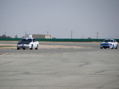 1992 Ford Taurus - Two cars compete on a sunny day at a race track.