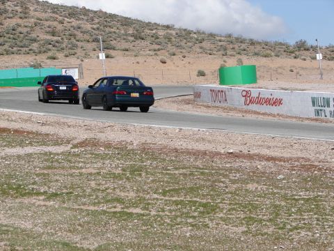 1992 Ford Taurus - A dark green sedan is seen from the rear on a race track, with another car ahead. The vehicle resembles a 1992 Ford Taurus.