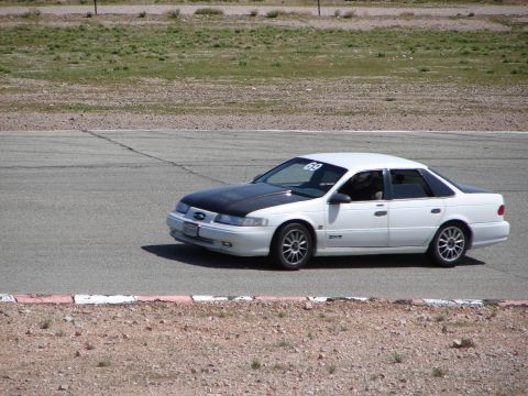 1992 Ford Taurus - A white 1992 Ford Taurus with a black hood is seen on a race track, displaying the number 69 on its windshield.