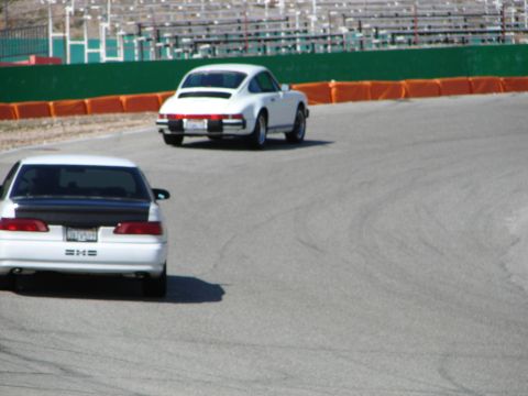 1992 Ford Taurus - Two cars race on a paved track with grandstands in the background.