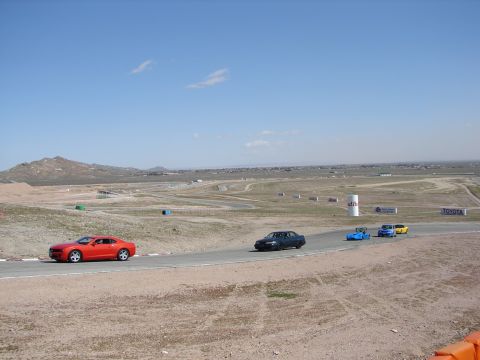 1992 Ford Taurus - A red sports car leads a group of vehicles on a race track under a clear blue sky.