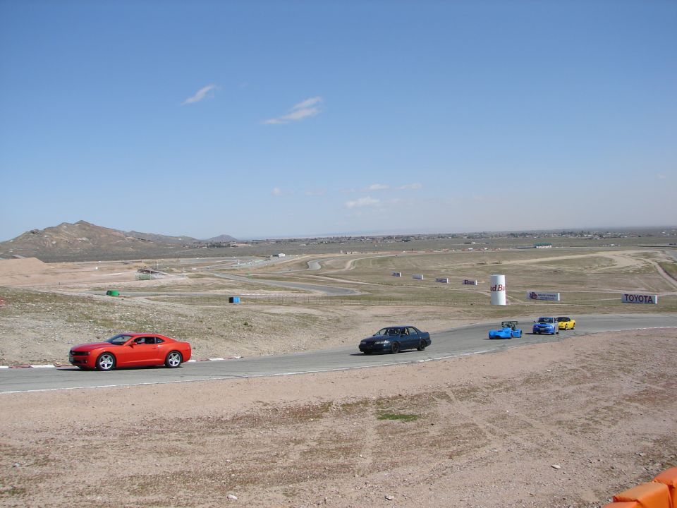 Red sports car on race track with other cars, mountains in background