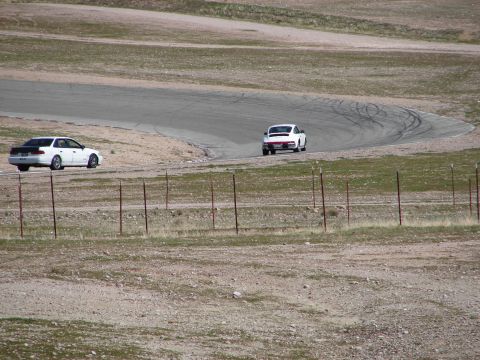 1992 Ford Taurus - Two cars, a white sedan and a white coupe, are seen on a race track during a sunny day.