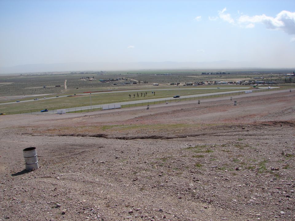 View of a race track with a few cars on it, distant buildings, and mountains in the background