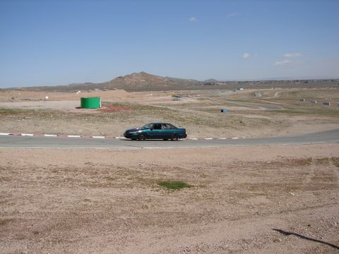 1992 Ford Taurus - A teal 1992 Ford Taurus sedan navigates a turn on a race track under a clear blue sky.