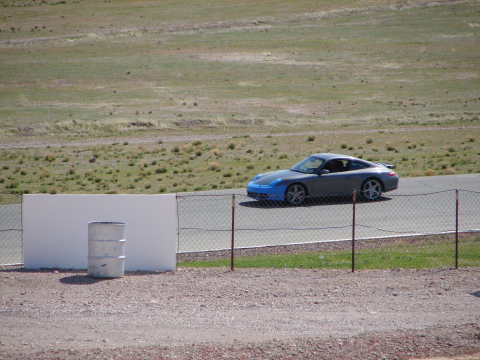 Gray Porsche 911 with blue front bumper on a racetrack, viewed from the side