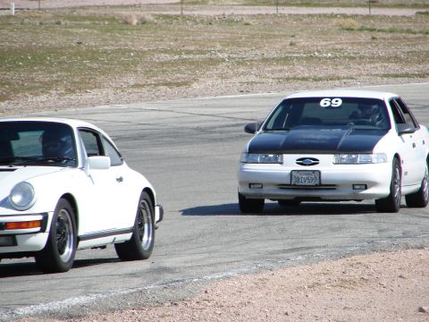 1992 Ford Taurus - A 1992 Ford Taurus and a Porsche compete on a paved racetrack under a clear sky.