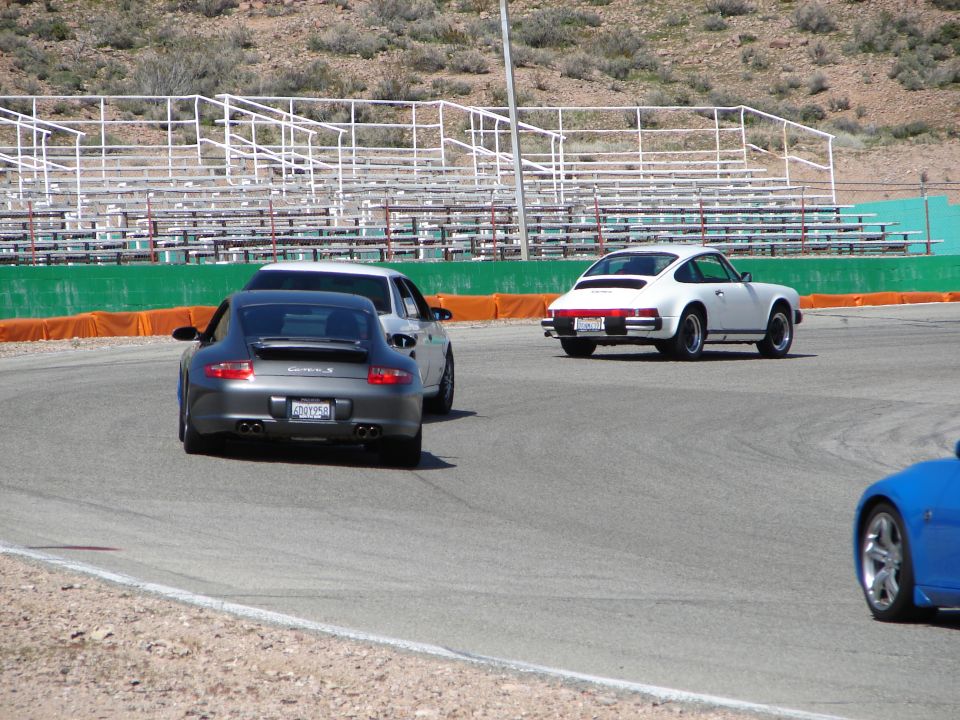 Gray Porsche 911 on a race track, rear view. White Porsche 911 in distance
