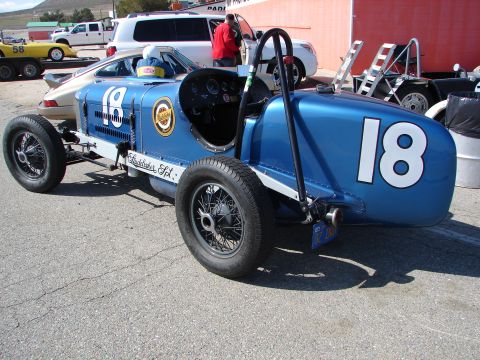 1992 Ford Taurus - A vintage blue race car, marked with the number 18, sits on pavement with other vehicles in the background.