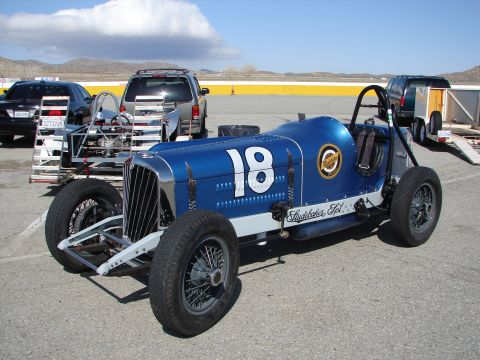 1992 Ford Taurus - A vintage blue race car, possibly a Studebaker special, is parked outdoors with other vehicles and a trailer.