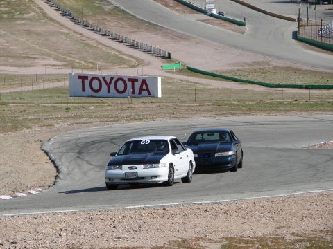1992 Ford Taurus - Two sedans compete on a race track, with a large Toyota advertisement visible in the distance.