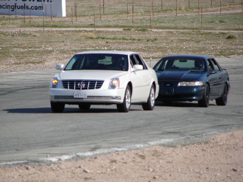 1992 Ford Taurus - A dark green sedan drives on a race track next to a white car.