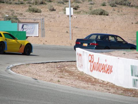 1992 Ford Taurus - A dark green sedan is on a race track next to a yellow sports car.