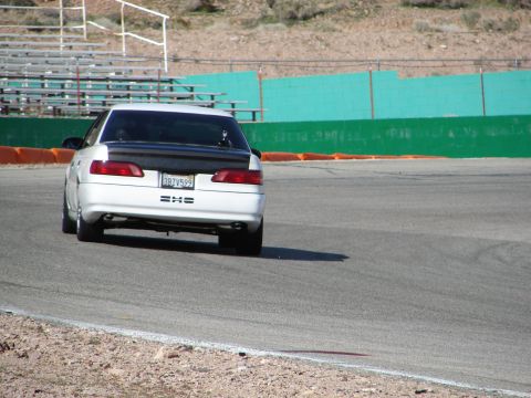 1992 Ford Taurus - A white sedan with a black spoiler drives on a racetrack.