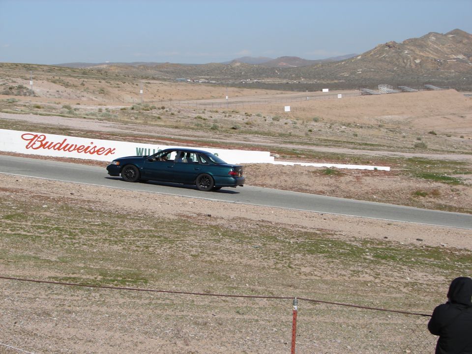 Teal Ford Taurus sedan on track at Willow Springs passing a Budweiser wall