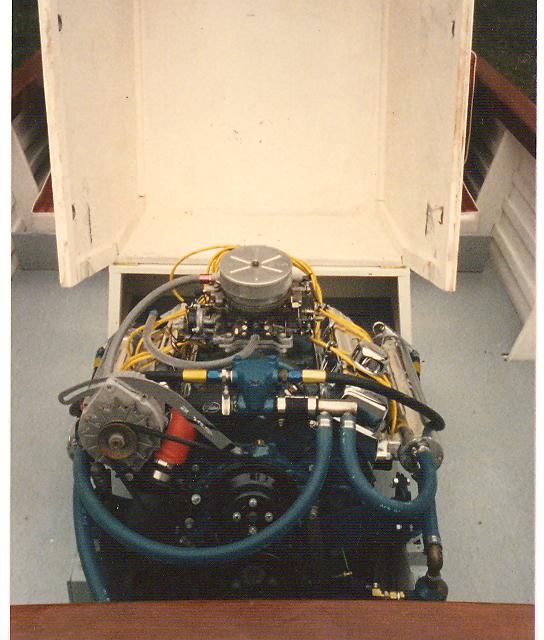Boat engine with blue hoses and yellow wires, viewed from above inside a white compartment