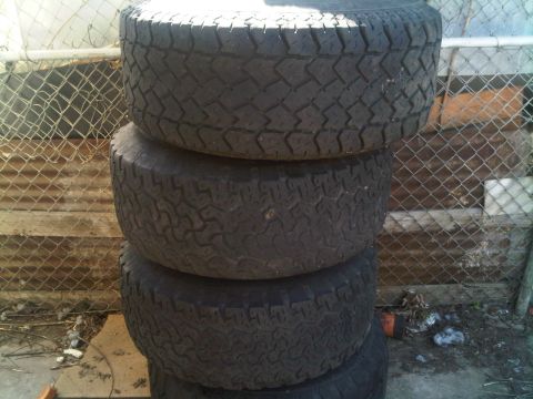 1985 Ford Bronco - Stack of four tires, likely for an off-road vehicle, with a chain-link fence in the background.