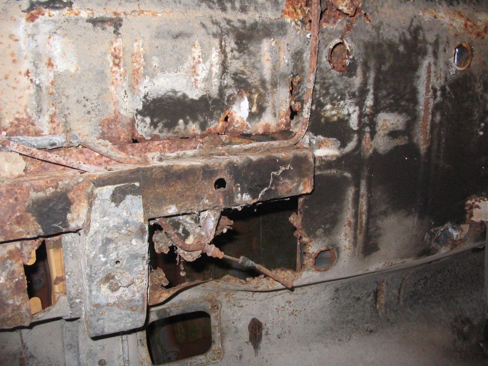 Heavily rusted metal frame with holes and exposed cables, showing significant corrosion