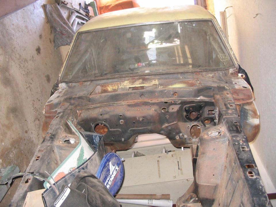 1970 Ford Mustang chassis, front view, showing engine bay and front frame rails. Car is rusty and appears to be undergoing restoration
