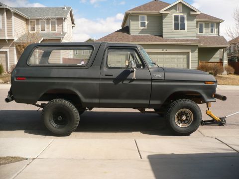 1979 Ford Bronco - A dark gray 1978 Ford Bronco is shown from the side, lifted on a jack in a suburban driveway.