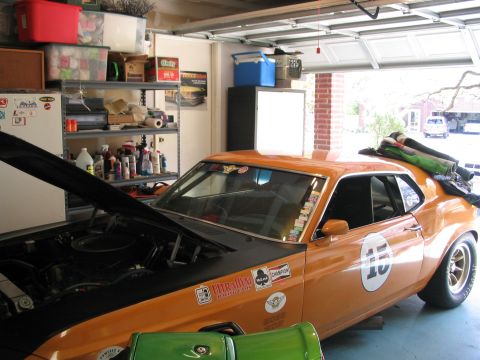 1970 Ford Mustang - Orange 1970 Ford Mustang race car parked in a garage with the hood up and covered in various decals.