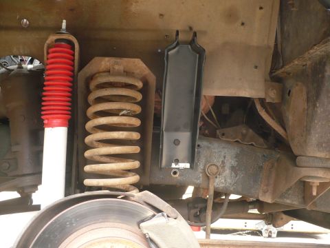 1979 Ford Bronco - Undercarriage view of a 1979 Ford Bronco, showing the suspension components including a red-booted shock absorber and a large coil spring.