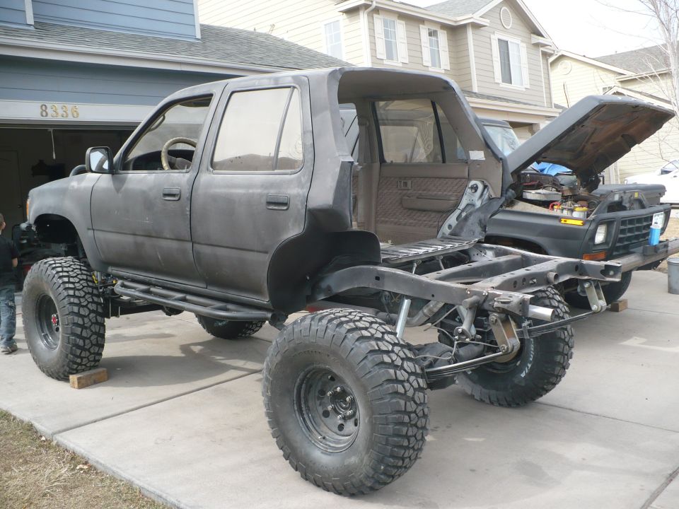 SUV body on a custom frame with large tires, another vehicle with hood up in background