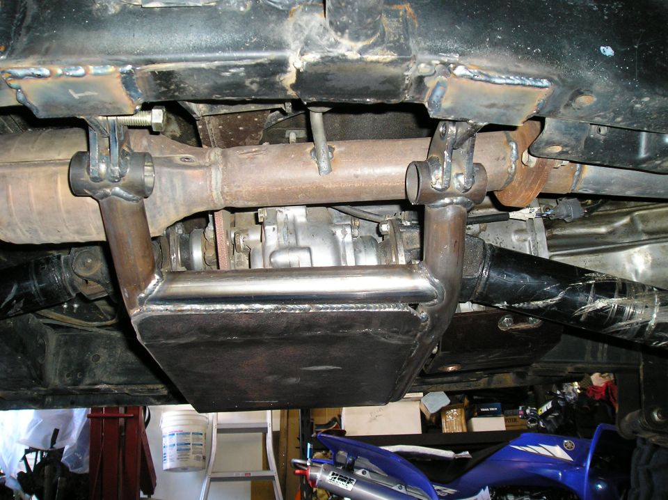 Custom metal skid plate bolted to vehicle frame near exhaust pipe and transfer case