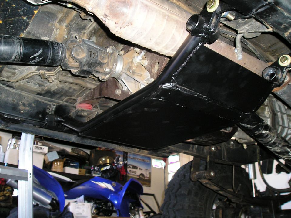 Undercarriage view of a vehicle's drivetrain with a black skid plate installed over the transfer case