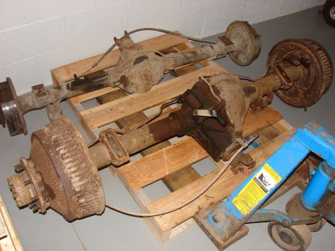 1996 Jeep Grand Cherokee - Two rusty rear axles with drum brakes are stored on pallets, with a blue jack nearby.
