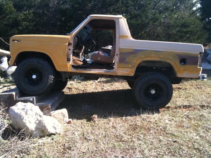 Yellow and tan Ford Bronco pickup truck with doors removed, sitting on concrete blocks
