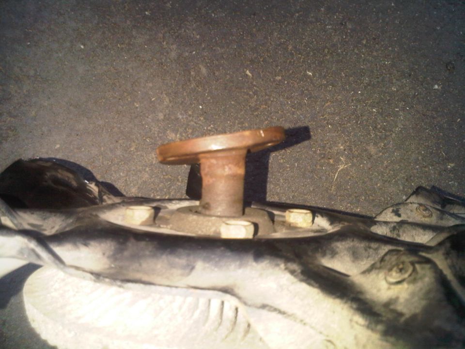 Rusted metal flange on a bolt protruding from a dark, metallic component with visible bolts