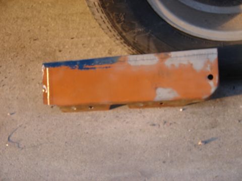 1973 Ford Ranchero - A detached car part, painted orange and blue, lies on the ground near a vehicle's tire.