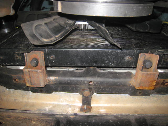 Underside view of a radiator, support brackets, and fan from below a truck
