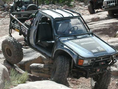 2002 Ford F-350 - This heavily modified pickup truck is shown off-roading over large rocks, with another vehicle visible in the background.