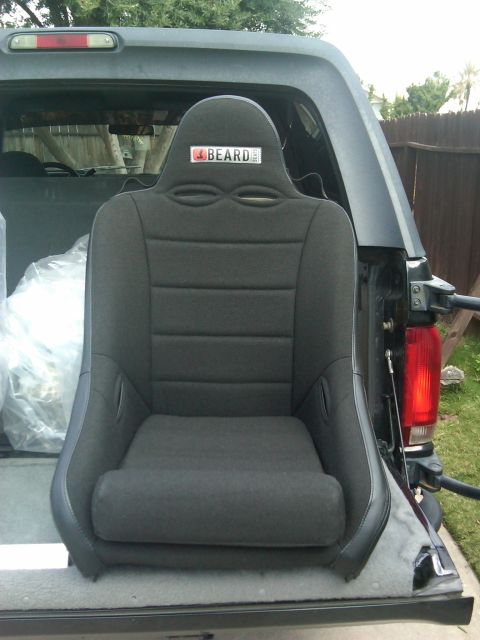 1986 Ford Bronco - A black racing seat with a BEARD logo is positioned in the rear of a dark-colored SUV.