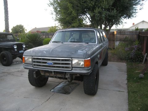 1986 Ford Bronco - A gray Ford Bronco is parked in a driveway next to a black Jeep, with trees and houses in the background.