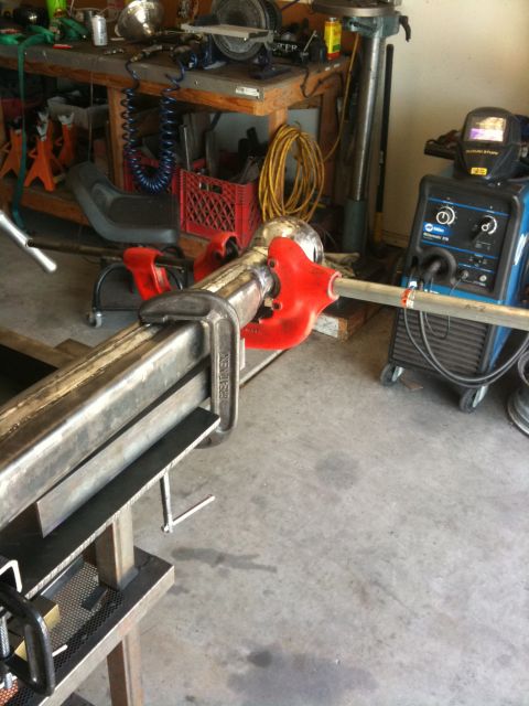 Suzuki Samurai - A pipe cutter is attached to metal tubing, with a welding machine and workbench visible in the garage setting.