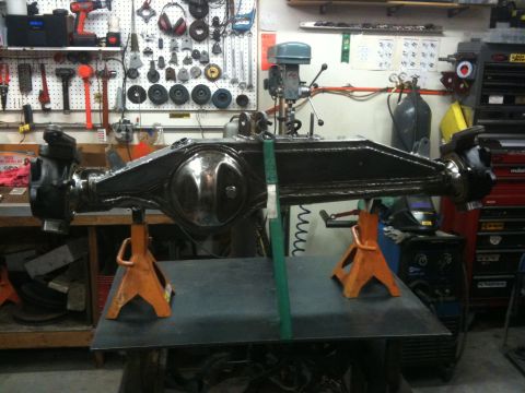 Suzuki Samurai - Front axle assembly, likely for a 4x4 vehicle, is supported by jack stands in a cluttered workshop environment.