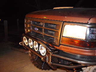 1993 Ford Bronco - Close-up of a brown Ford truck's front end at night, a custom bumper with multiple lights.