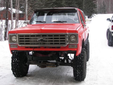 1990 Chevrolet Suburban - This lifted red Chevrolet K5 Blazer is shown from the front in a snowy environment, with another vehicle partially visible to the right.