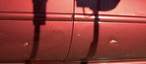 1997 Ford Taurus - Close-up of a red car's side door, showing minor damage and a dusty surface.