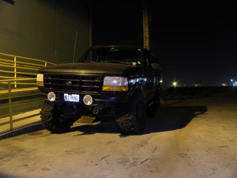 1995 Ford Bronco - A lifted black Ford Bronco is parked outdoors at night under artificial lighting.