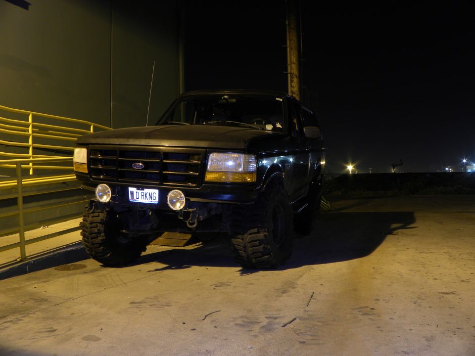 Black Ford Bronco parked at night, lifted with large tires. License plate reads 'DRKNG'