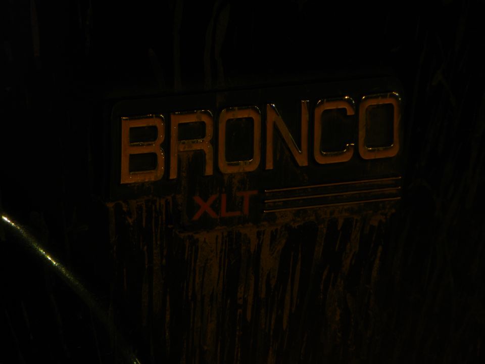 Bronco XLT badge on a dark vehicle, covered in dirt and water streaks