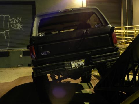 1995 Ford Bronco - The rear of a black Ford Bronco is visible, parked in front of a garage door with graffiti.