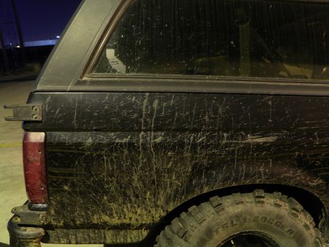 1995 Ford Bronco - Mud-splattered black SUV with a camper shell is seen from the side, revealing its rear tail light and tire.