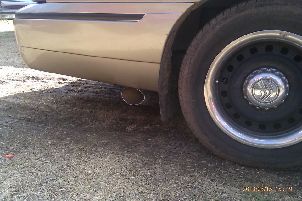 Gold full-size sedan rear quarter with chrome dual exhaust tip and steel wheel with Mercury hubcap