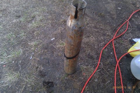 2000 Mercury Grand Marquis - A rusted metal cylinder with a black strap is lying on the ground next to a red cable.