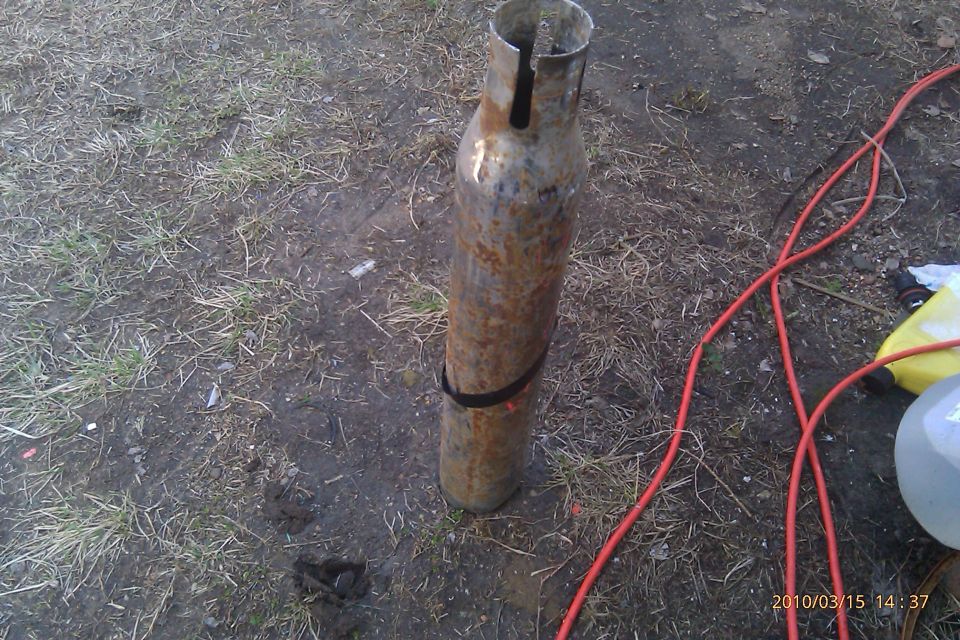 rusted metal cylinder with black strap on the ground, red cable nearby